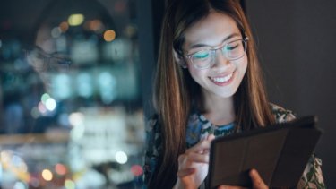 A smiling girl who removes her eyeglasses and looking to her laptop