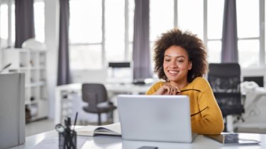 A smiling girl who removes her eyeglasses and looking to her laptop